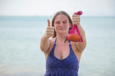 Portrait of woman holding ice cream against sea