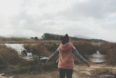 Rear view of carefree woman standing on field against sky