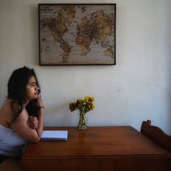 Woman sitting on table against wall at home