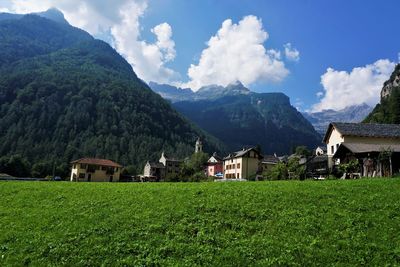 Scenic view of field by houses and mountains against sky