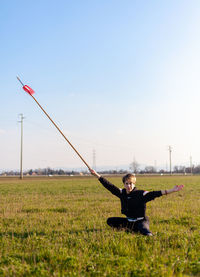 Caucasian young woman practicing wushu martial art on a green meadow with a long spear