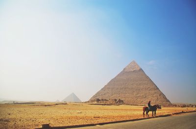 Man riding horse by great pyramid of giza against sky