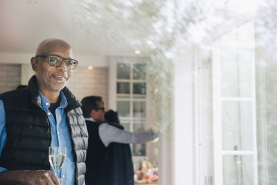 Portrait of smiling senior man holding drink seen through window