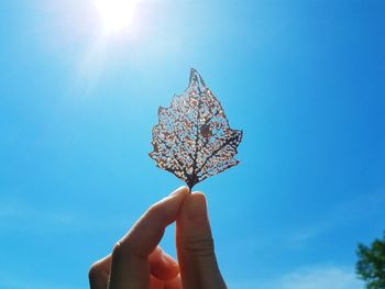 Low angle view of hand holding umbrella against blue sky