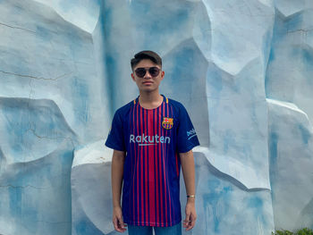 Portrait of man wearing sunglasses standing against blue wall