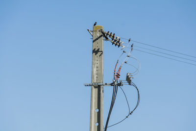 Low angle view of electricity pylon against clear blue sky