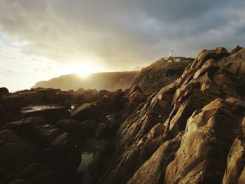 Distant view of mossel bay lighthouse on rocky mountains against cloudy sky