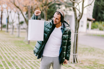 Mid adult man holding bag looking away while standing outdoors