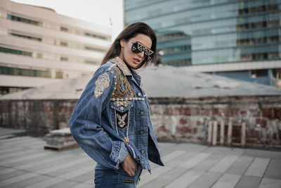 Young woman wearing sunglasses while standing against building in city