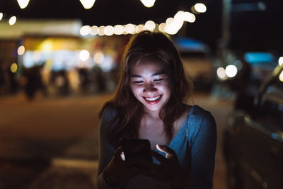 Portrait of smiling woman using mobile phone at night
