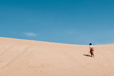 Woman walking on sand dune in desert against sky