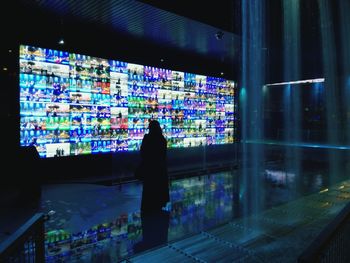 Rear view of silhouette man looking at illuminated store