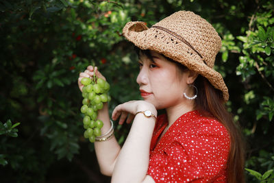 Young woman holding grapes while looking away against plants