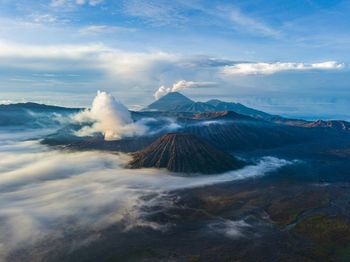 Smoke emitting from volcanic landscape against cloudy sky