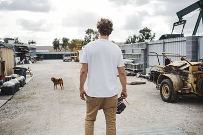 Rear view of carpenter looking at dog while standing outside workshop