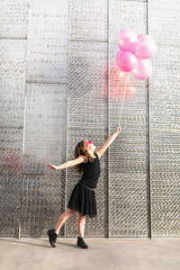 Young girl with pink glasses & pink balloons in front of a metal wall.