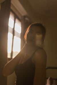 Portrait of young woman while standing by window at home