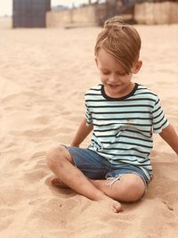 Smiling cute boy sitting on sand at beach