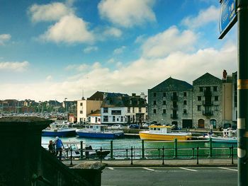 Boats moored at harbor against sky in city