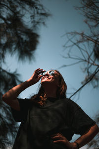 Low angle view of woman wearing sunglasses standing against clear sky