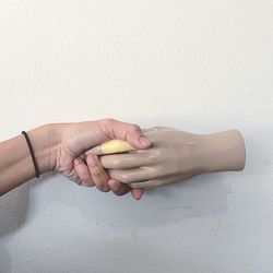 Cropped image of person holding artificial hand against wall