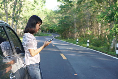 Low section of person holding smart phone while standing on road