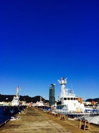 Boats in harbor against clear blue sky