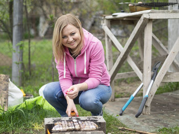 Portrait of smiling woman preparing food on barbecue outdoors