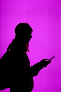 Side view of silhouette woman using phone against pink background
