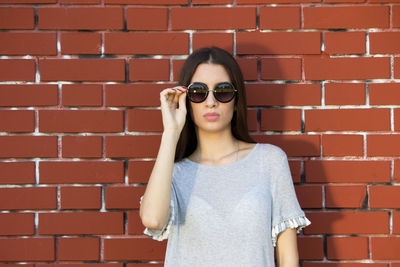 Portrait of young woman wearing sunglasses against brick wall