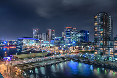 Illuminated buildings by river against sky in city at night