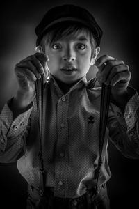 Portrait of boy wearing suspenders while standing against black background