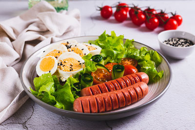 Fried sausages, tomatoes, lettuce and a sandwich with a boiled egg on a plate on the table