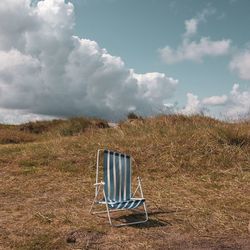 Empty chair on field against sky