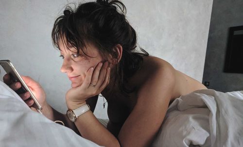 Smiling woman using mobile phone while lying on bed at home