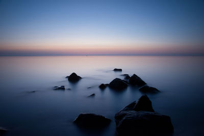 Rocks in sea against sky at sunset