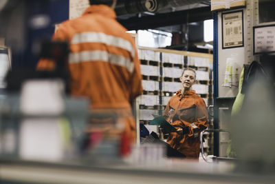 Female worker in uniform discussing with male coworker in factory