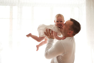 Father and daughter laughing on light window, toddler on hands. happy loving family.
