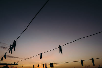 Silhouette clothespins hanging on clotheslines against sky during sunset