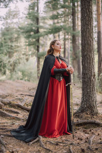 Full length of young woman holding sword while standing in forest