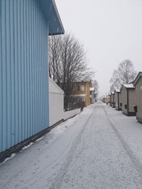 Snow covered road by building against sky