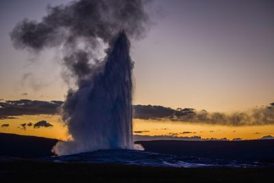 Waves splashing on shore against sky during sunset