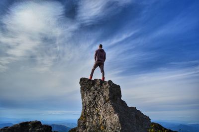 Low angle view of man standing on rock against sky