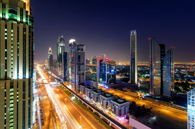 Illuminated modern buildings in city against sky at night