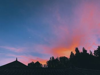 Silhouette trees and houses against sky during sunset