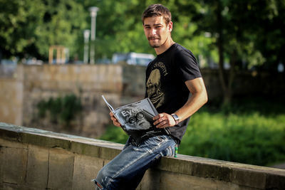 Portrait of young man sitting on retaining wall