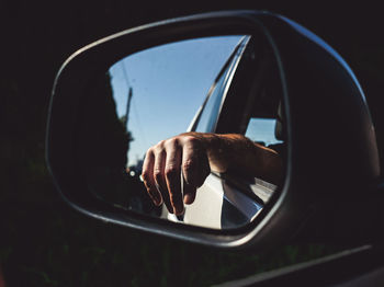 Close-up of hand in side-view mirror of car