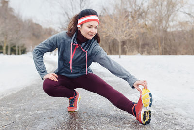 Full length of woman exercising on road during winter