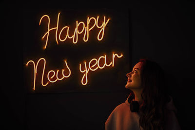 Profile of beautiful girl in headphones at night against back of glowing orange inscription new year