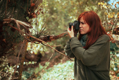 Young woman photographing with camera while standing in forest